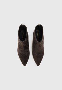 Botas de ante marrón hasta el tobillo con un diseño de punta puntiaguda, cremalleras en la parte trasera, textura suave y un estilo minimalista. Nombre de la marca en las plantillas.