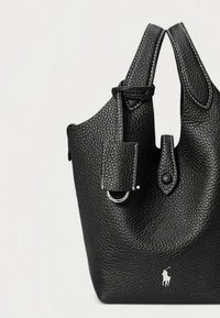 Black pebbled leather handbag with double top handles, a small detachable tag, and a silver logo accent at the base. Features textured surface.