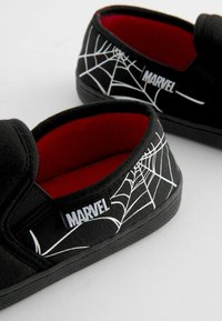 Pantofole nere in tela con una fodera rossa. Presentano un design di ragnatela bianca e un'etichetta "MARVEL" sul lato. Design slip-on a profilo basso.