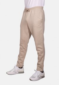Pantaloni jogger beige realizzati in tessuto morbido, con una vita elastica dotata di cordoncino, tasche laterali e un design a gamba affusolata.