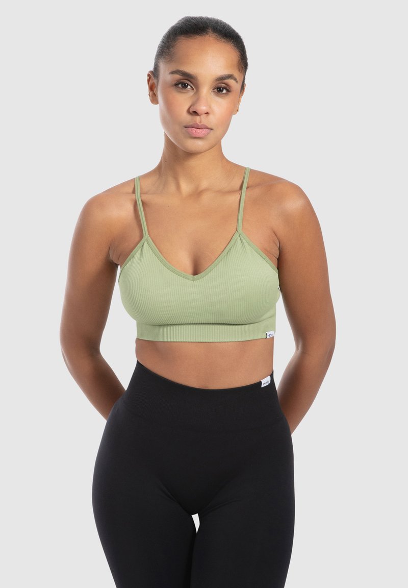 Bralette de canalé verde claro con escote en V y tirantes finos, combinado con leggings negros de tiro alto. Textura suave y diseño ajustado.