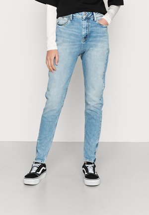 Jeans de cintura alta azul claro com um corte slim e textura desbotada. Combinados com ténis pretos com atacadores brancos e riscas laterais.