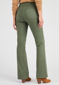 Olijfgroene flared broek met vijf zakken, textuurstof en hoge taille. Gecombineerd met bruine enkellaarsjes met hak voor contrast.