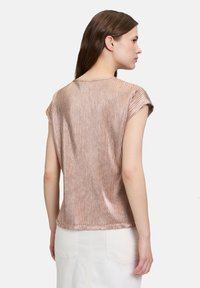 Rosa-goldener, gerippter Kurzarmoberteil mit lockerem Schnitt. Verfügt über einen runden Ausschnitt und einen subtilen Glanz auf einer glatten Textur.