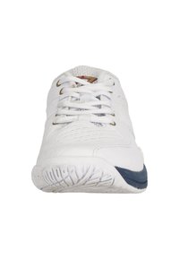 Vit sportssko med övre i mesh, vadderad tunga och snören. Har en texturerad gummisula med en blå accent nära hälen.