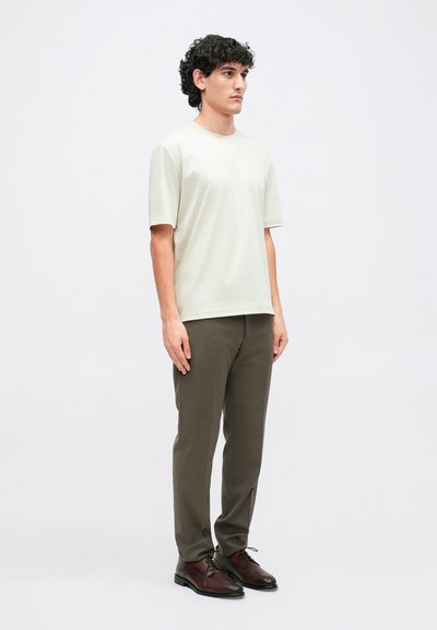 Világos bézs rövidujjú póló, olíva zöld nadrággal és barna fűzős cipővel párosítva, ami egy egyszerű, hétköznapi ruházatot mutat be.