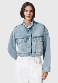 Chaqueta de mezclilla recortada en azul claro, con dos bolsillos en el pecho, cuello deshilachado y botones plateados. Textura suave, corte relajado.