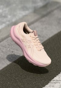 Hellrosa Laufschuh mit strukturierter Oberseite, gepolsterter pinkfarbener Sohle und dünnen weißen Akzenten. Verfügt über Schnürsenkel und Perforationen für Atmungsaktivität.