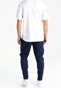 White short-sleeve shirt with black accents and navy sweatpants. The outfit is paired with white sneakers, featuring a smooth texture and athletic fit.