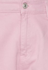 Hellrosa Denimstoff mit klassischem Fünf-Taschen-Design, Metallknöpfen und dezentem Texturmuster mit sichtbaren diagonalen Webstrukturen.