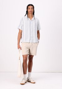 Short-sleeve, light blue striped shirt with a pocket, beige corduroy shorts, and a cream tote bag. Beige sneakers with white soles.