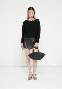 Cardigan nero a maglia con chiusura a bottoni, abbinato a una gonna di pelle nera. Tiene in mano una borsa nera testurizzata con due manici.