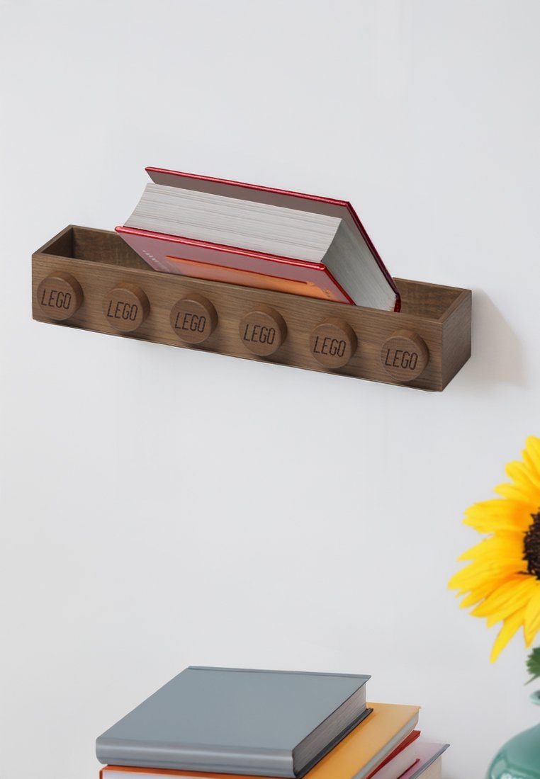 Houten wandplank die grote LEGO-blokken nabootst, bevat een rood gebonden boek, met hieronder gestapelde boeken en een gele zonnebloem.
