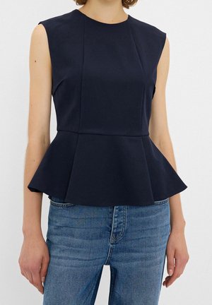 Sleeveless navy peplum top worn with blue jeans, showing upper body and arms against a plain white background.