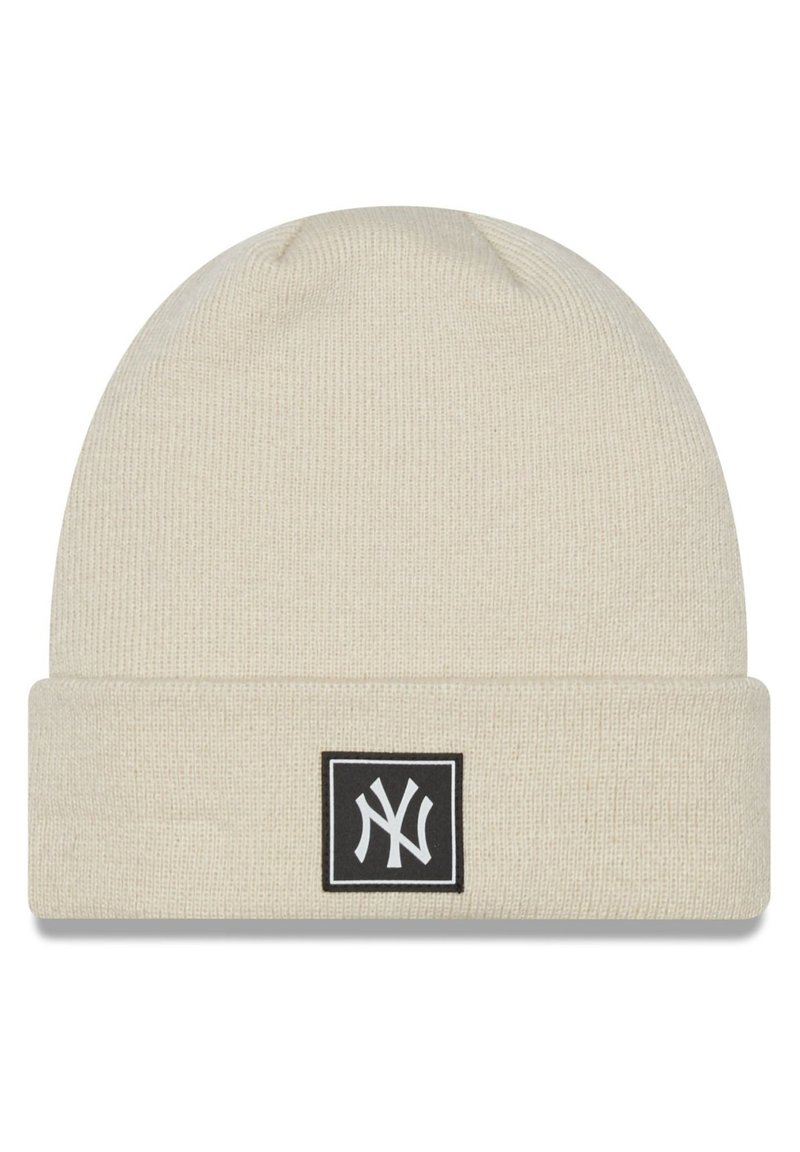 Cream knitted beanie with a folded cuff, featuring a black square patch displaying a white logo. Soft texture, ribbed pattern.