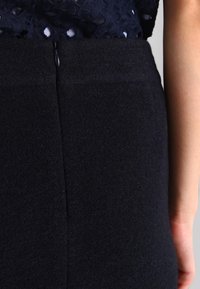 Jupe crayon en mélange de laine de couleur bleu marine, présentant une texture lisse, une fente au dos et une fermeture éclair discrète. Design minimaliste avec des lignes épurées.