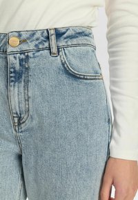 Vaqueros de mezclilla de cintura alta azul claro con costuras visibles, cierre de botón en la parte delantera y un diseño clásico de 5 bolsillos.