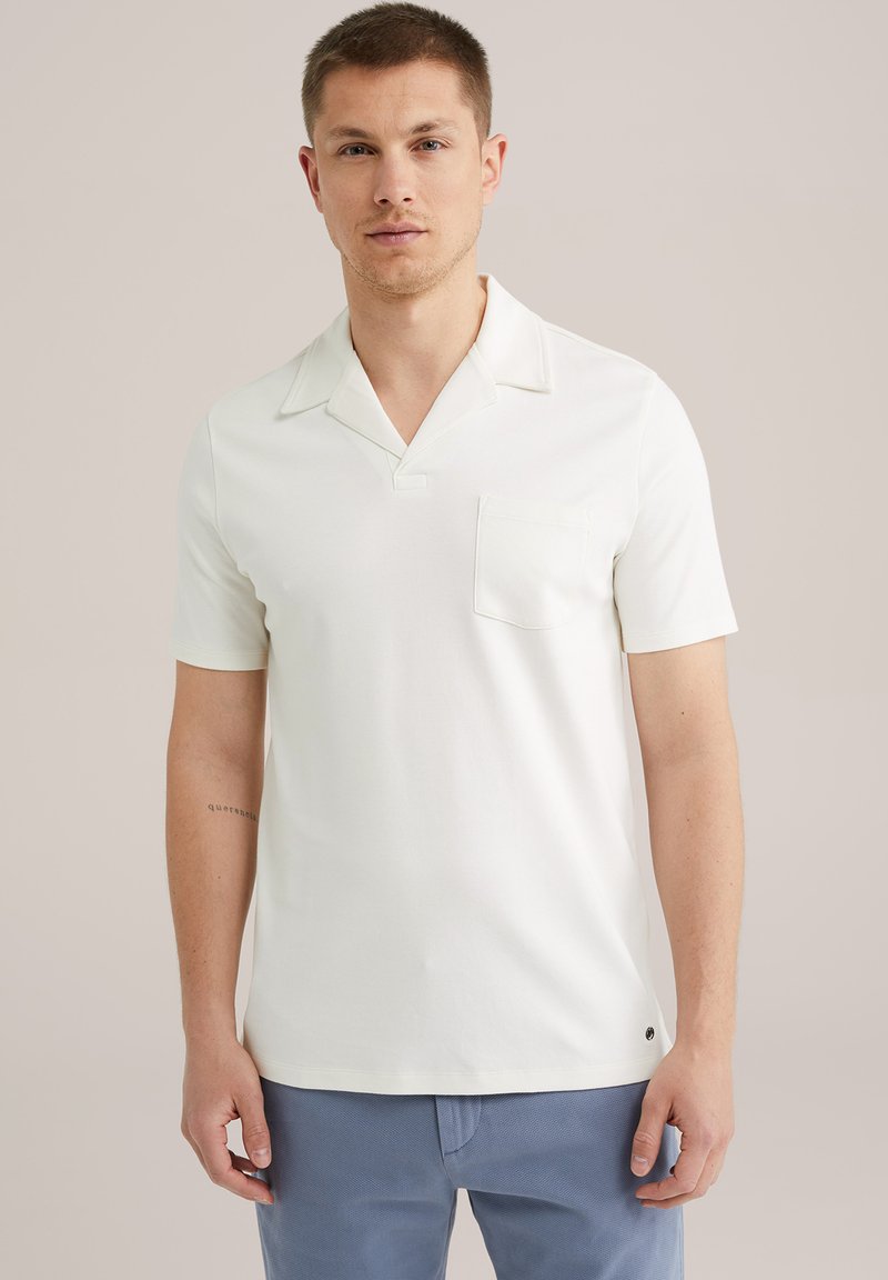 Polo alb cu mânecă scurtă dintr-un material moale, având guler în V, și un singur buzunar pe piept. Branding subtil la tiv.