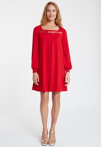 Rotes knielanges Kleid mit langen, gepufften Ärmeln. Verfügt über einen quadratischen Ausschnitt mit transparenter Einlage und goldenen Hardware-Details an der Brust.