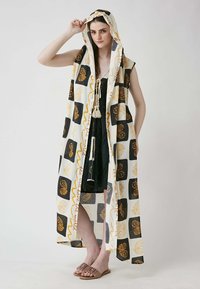 Long, patterned cardigan with a hood in cream, black, and gold, featuring floral designs and tassel detailing; lightweight fabric.