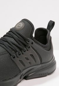 Černá atletická bota s texturovaným svrškem, šněrovacím designem a výrazným logem. Gumová podrážka s masivním, měkkým stylem.