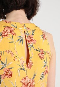 Yellow floral dress with a keyhole back detail, featuring pink and white flowers with green leaves and a smooth, lightweight fabric.