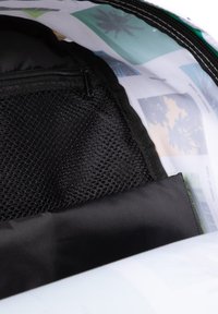 Svart nätficka inuti en väska, med ett slätt strukturerat svart lock och en mönstrad foder med bilder av palmer och landskap.