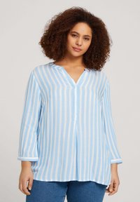 Blusa a rayas azul claro y blanca con cuello en V, mangas largas y un corte holgado. Fabricada en un tejido suave, presenta un detalle de botón en el cuello.