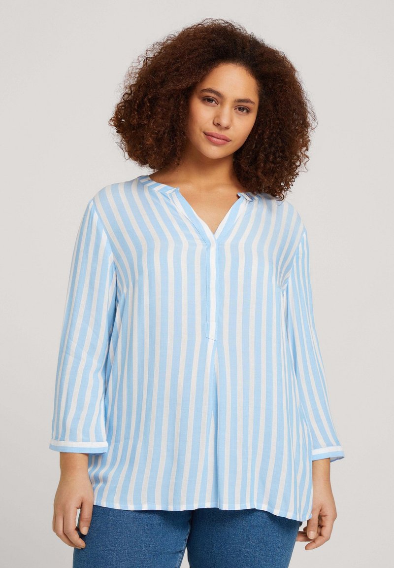 Blusa a rayas azul claro y blanca con cuello en V, mangas largas y un corte holgado. Fabricada en un tejido suave, presenta un detalle de botón en el cuello.