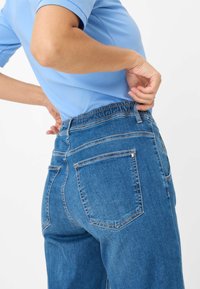 Blauwe spijkerbroek met een aansluitende taille en elastische band. Heeft achterzakken en een licht taps toelopende pijpdesign. Gladde textuur.