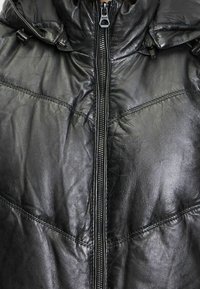 Czarna skórzana kurtka z zamkiem błyskawicznym z przodu, ocieplaną kapturem i pikowaną fakturą. Posiada widoczne przeszycia i ozdobne elementy metalowe.