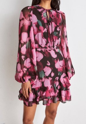 Kvinde iført en langærmet, blomsterprydet pink og sort flæset minikjole med nøglehulsudskæring og puffede ærmer.