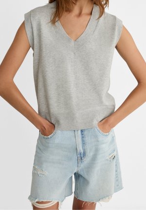 Woman wearing a sleeveless gray knit vest with a V-neck and light blue distressed denim shorts with frayed hems and pockets.