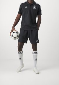 Černý fotbalový komplet Adidas obsahující polo triko s bílými pruhy, šortky, pruhované ponožky po kolena a černobílý fotbalový míč.