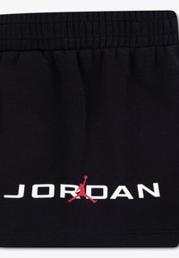 Μαύρο σορτς από μπλέντ βαμβακιού με ελαστική μέση. Λευκό κείμενο "JORDAN" και κόκκινο λογότυπο Jumpman εκτυπωμένα μπροστά.