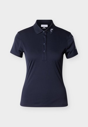 Tamsiai mėlynas polo marškinėlis iš lygaus audinio. Turi apykaklę, tris sagas ir išsiuvinėtą logotipą ant apykaklės bei rankovės. Trumpomis rankovėmis.