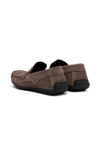 Mocasines de ante marrón con parte trasera baja, que presentan una superficie texturizada y una suela de goma negra contrastante para mayor agarre. Diseño simple y limpio.