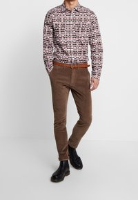 Langärmlig patroonhemd in bruin, wit en oranje; gecombineerd met bruine corduroy broek en zwarte leren enkellaarzen.