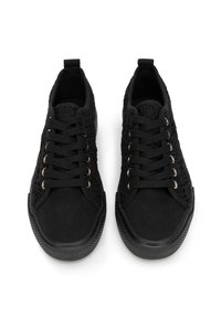 Zapatillas negras con un diseño de cordones, parte superior texturizada con patrones similares al ganchillo y una suela de goma lisa. Ojales dorados acentúan los cordones.