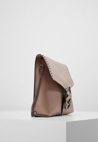 Mjukt rosa läderhandväska med klaffstängning, silverkedjesnor och nitar längs kanten. Har en cirkulär metallisk detalj.