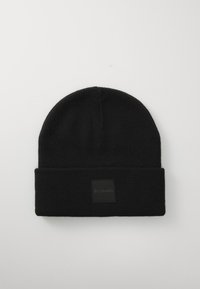 Black knit beanie featuring a folded cuff and a square black fabric patch with the Columbia logo. Smooth texture, simple design.