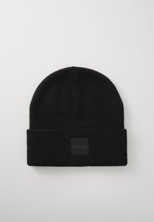 Schwarze Strickmütze mit umgeschlagenem Saum und einem quadratischen schwarzen Stoffpatch mit dem Columbia-Logo. Glatte Textur, schlichtes Design.
