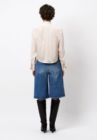 Beige blouse with a high neckline, paired with blue denim culottes. Model wears knee-high glossy black boots. Textured fabric details visible.