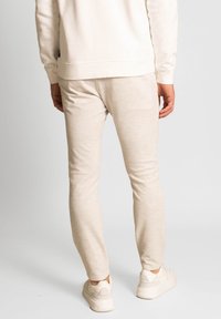 Béžové tepláky vyrobené z měkké tkaniny, mají slim fit a elastický pas. Nosené s světlými teniskami.