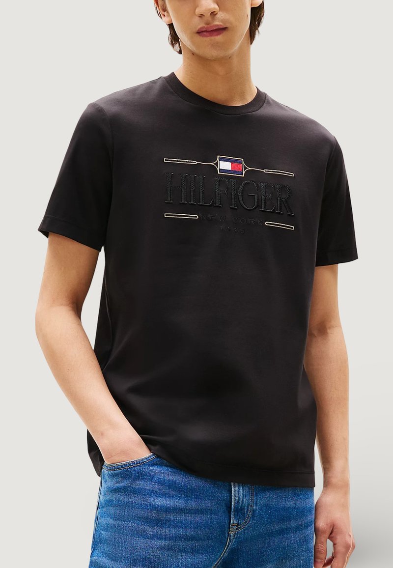 T-shirt nera in cotone con logo "HILFIGER" ricamato, maniche corte e collo rotondo, abbinata a jeans di denim blu.