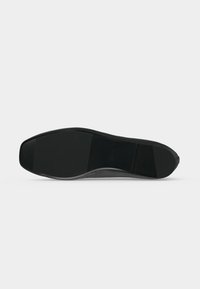 Semelle de chaussure noire à texture lisse et forme légèrement carrée à l’avant, présentée à plat sur un fond clair.