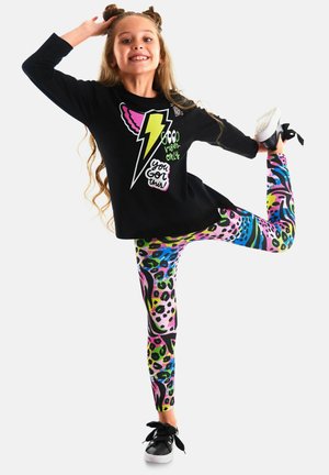 Zwarte lange mouwen top met kleurrijke bliksemafbeelding en tekst, gecombineerd met levendige multi-patroon leggings met vlekken en wervelingen.