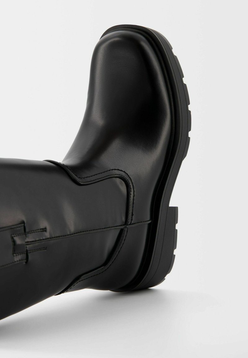 Stivale alla caviglia in pelle nera con punta tonda, texture morbida, dettagli delle cuciture laterali e suola in gomma chunky per una buona aderenza.