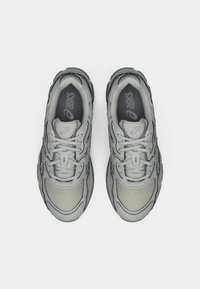 Sive atletske copate z mrežastim in sintetičnim zgornjem delom, zaobljene oblike, z reliefnimi detajli in oblazinjeno jezičko. Črn podplat.