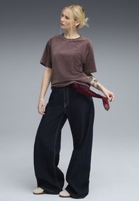 Lilla ribbet t-shirt, vide mørke denim bukser, rød leopardmønstret tørklæde bundet om taljen og lyse sko.